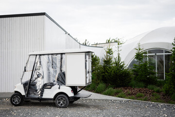 White utility golf cart parked near modern building and landscaped greenery