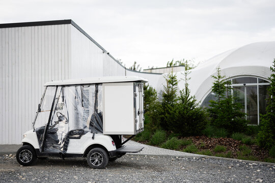 White utility golf cart parked near modern building and landscaped greenery