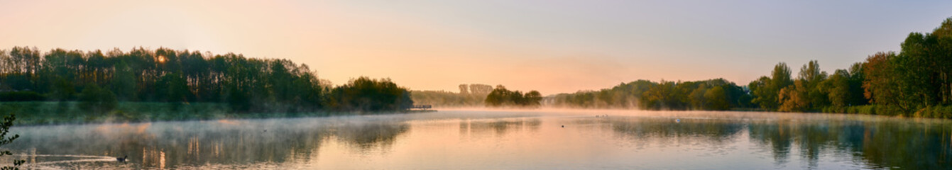 Obraz premium Panoramic shot of a lake surrounded by forests under a sunset sky