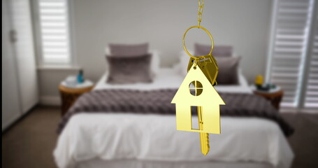 Hanging gold house-shaped key fob with metal keys in bedroom, highlighting neat bed and pillows