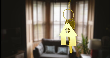 Hanging golden key ring with house-shaped keychain and keys in living room, with sofa and lamp