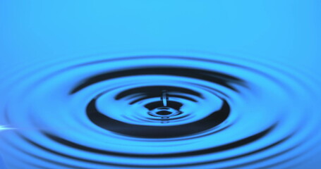 Capturing water droplet creating concentric ripples on reflective water surface in studio
