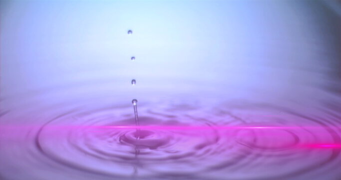 Hovering water droplet creating ripples on liquid surface at studio, with neon-pink reflection line