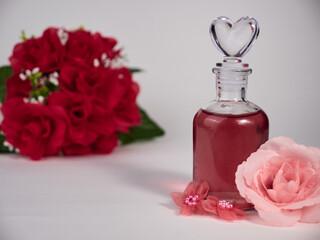 Closeup of a glass bottle of perfume with artificial pink roses on the white background