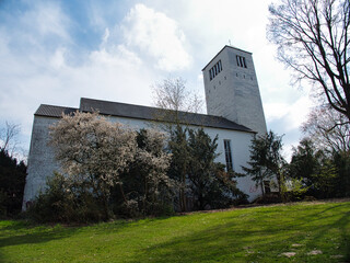 Low angle shot of a small white church surrounded by trees and grass under a bright cloudy sky
