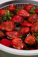 Close-up of ripe strawberries soaking in water inside a colander. The glossy surface of the berries and reflections create a fresh and appetizing look.