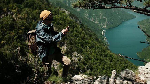 Female traveler takes photo or video using smartphone at Banjska stena viewpoint in Tara National Park, Serbia. Panoramic view of Drina river canyon and lush green mountains. Solo travel concept