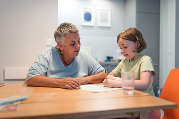 A portrait of grandmother and granddaughter doing homework together at home.
