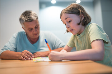 A portrait of grandmother and granddaughter doing homework together at home.	
