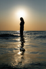 silhouette of young slim woman in front of the sun on a calm beach