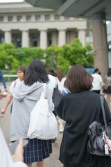 In early summer in Shanghai, near The Bund, Japanese high school girls in uniforms walk through a crowd, seen from behind, their presence adding youthful energy to the city's lively atmosphere.