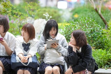 In early summer in Shanghai, near The Bund, Japanese high school girls in uniforms sit at a street corner, chatting and laughing, their smiles adding a touch of youth to the vibrant city atmosphere.