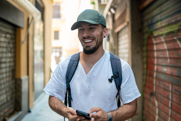 Tourist using smartphone and smiling in city alley