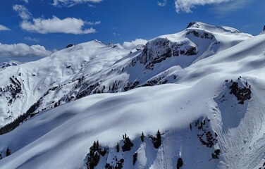 Snowy mountain range under a bright blue sky with scattered clouds on a clear sunny winter day