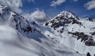 Aerial view of snow covered mountain range with scattered trees under a partly cloudy blue sky day