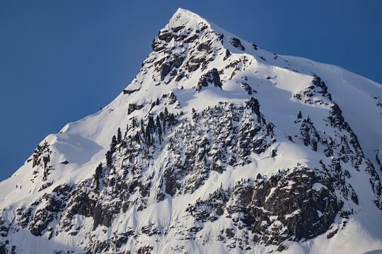 A view of a snow covered mountain peak against a clear blue sky on a bright sunny day in winter - Powered by Adobe