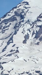 A detailed view of a snow covered mountain with visible rock formations under a clear blue sky above