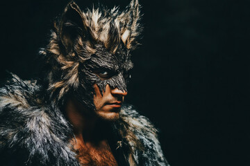 Caucasian actor wearing wolf mask and fur is posing on a dark background for a Halloween or fantasy photoshoot