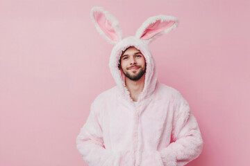 Cheerful man smiling while wearing a funny pink bunny costume, posing playfully against a vibrant pink background