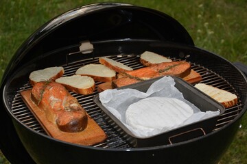  Grilled salmon fillets and sliced bread on charcoal BBQ grill with cedar plank and cheese