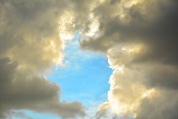 Bright blue sky opening between dense clouds with sunlight highlighting dramatic textures