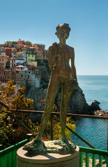 A bronze statue of a woman holding grapes stands prominently against the of colorful houses of Manarola, Cinque Terre