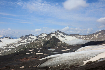 Panoramic View Of A Mountain Range With Snow Patches, A Large Glacier, And Dark Volcanic Soil Or...