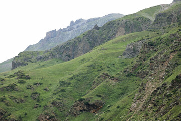 Scenic View Of Lush Green Mountain Slopes With Exposed Rocky Outcrops And Ridges Under A Hazy Sky....