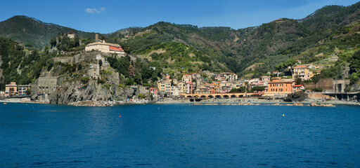 panoramic view of Monterosso al Mare, Cinque Terre, the seaside village with colorful buildings, towers, nestled between terraced cliffs above the blue waters of the Ligurian Sea.
