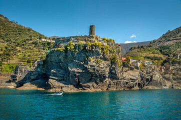 The seaside village on rocks of Monterosso al Mare, Cinque Terre, towers of a medieval fortress, and colorful houses nestled between terraced hills