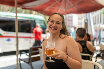Tourist smiling and drinking beer at outdoor cafe with tour bus in background