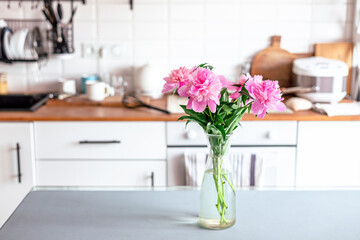 Vase with peonies flowers on dining table in kitchen