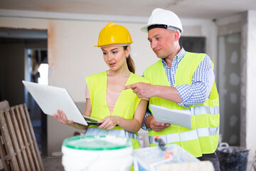 Man and woman builders talking about repair works in apartment. Pointing finger gesture.