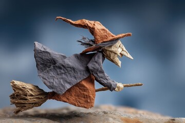Origami witch figure with pointed hat and broom, crafted from textured paper, flying against a blue background, creative, handmade, Halloween, fantasy, magical, artistic, whimsical, folklore.