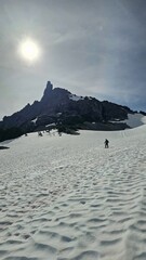 Person hiking on a snow covered field towards a rocky mountain under a bright sunny sky outdoor view
