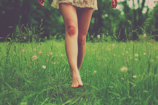 Woman walking barefoot through tall grass on a sunny day in a lush green meadow