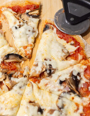 Mushroom pizza on wood cutting board, pizza cutter at edge. whole wheat pizza dough.
