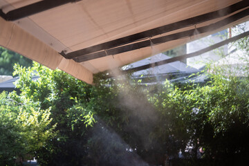 Automatic mist nozzle water spraying system to make humidifier and cooling climate to reduce hot weather. Water fog machine working during hot summer day. Refreshes plants and cleaning air outdoors