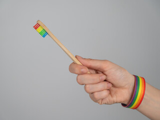 Woman wearing bracelet holds toothbrush with rainbow flag. 