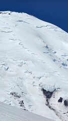 A view of a snow covered mountain under a clear blue sky with visible crevasses and rock formations