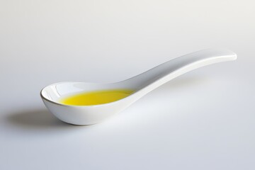 In a white ceramic spoon is a spoonful of light yellow liquid that may be oil or sauce