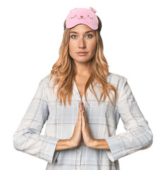 Blonde in pajamas with sleep mask praying, showing devotion, religious person looking for divine...