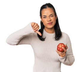 Young Filipina holding a tomato showing a dislike gesture, thumbs down. Disagreement concept.