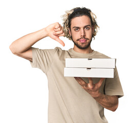 Young man holds pizza boxes for delivery showing a dislike gesture, thumbs down. Disagreement...