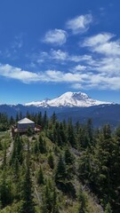 Aerial view of a wooden structure on a forested hilltop with a snow capped mountain in the distance