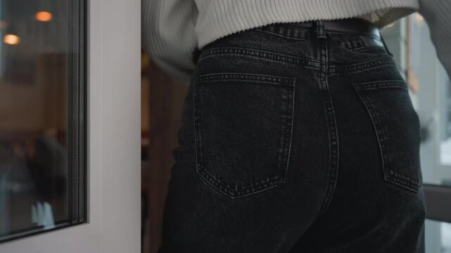 close up of young woman in ribbed white sweater opening glass door while entering mall, capturing gentle grip on curved white handle with natural daylight and blurred reflections in background