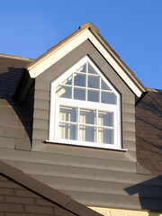 Triangular dormer window with slate cladding and black roof tiles under blue sky