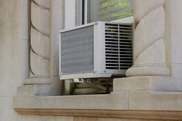 exterior view of air conditioning window unit extruding from the window sill with a portable safety...