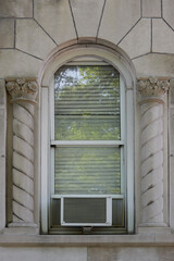 exterior view of air conditioning window unit extruding from the window sill with  elegant, decorative molded concrete architectural details, with a portable safety ledge support installed under it