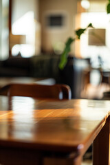 A warm, sunlit dining room with a focus on the wood table, blurred interior with furniture and plants in the background, elegant and inviting.